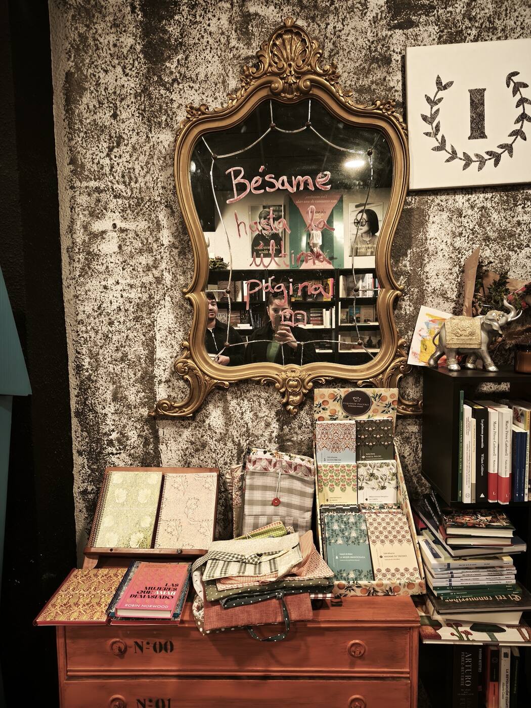 Espejo dorado con el letrero «Bésame» y el cartel de la I, sobre una cómoda con libros