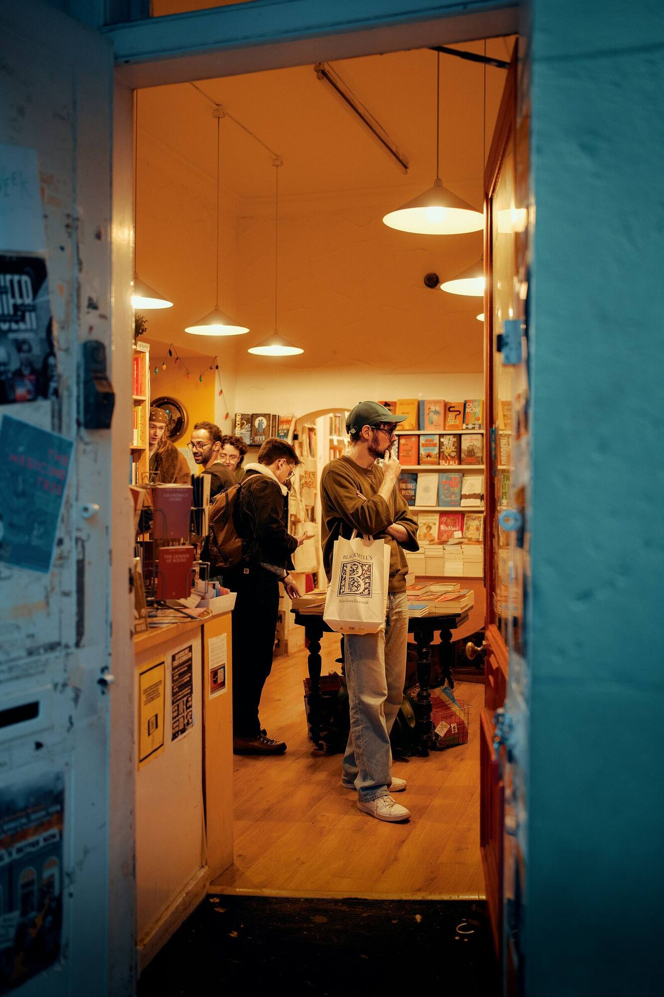 Gente mirando libros en una librería cálida, vista desde la puerta